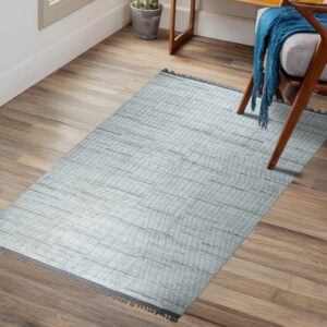 Gridded light blue rug rests on wood floors beside a modern armchair draped with a bright blue throw.