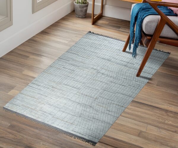 Gridded light blue rug rests on wood floors beside a modern armchair draped with a bright blue throw.