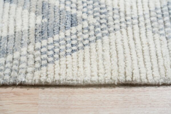 High-pile rug texture showing thick off-white and lower blue-gray carved sections on light wood flooring.