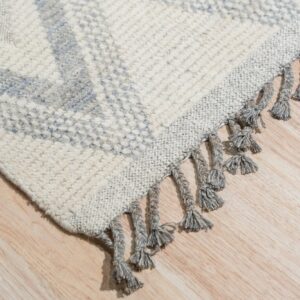 Cream and blue textured rug featuring a geometric pattern and thick gray tassels on a wood floor.