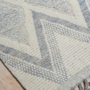 Textured cream and gray geometric rug with tassels lying on light wood plank flooring.