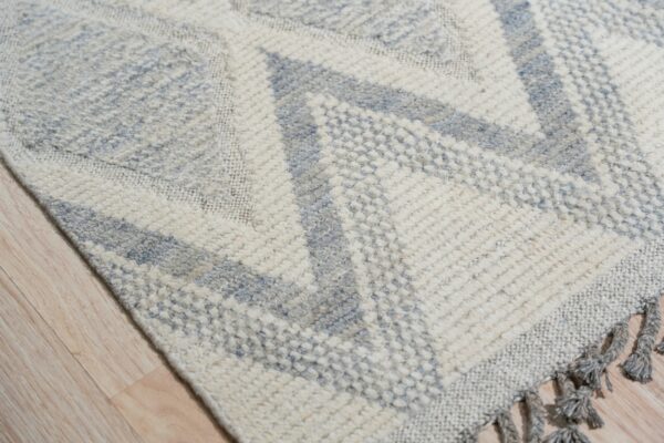 Textured cream and gray geometric rug with tassels lying on light wood plank flooring.