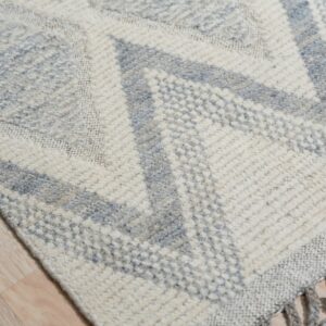 Geometric cream and pale blue textured rug detail showing knotted fringes on light hardwood.