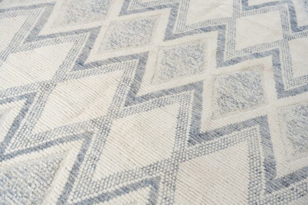 Textured off-white rug with geometric dusty blue zigzag lines and diamond shapes.