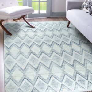 Textured beige rug with blue chevron and diamond patterns displayed between a white chair and gray sofa.