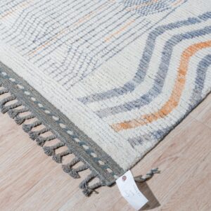 Textured cream rug featuring blue and orange wavy stripes, a gray border, and thick knotted tassels.