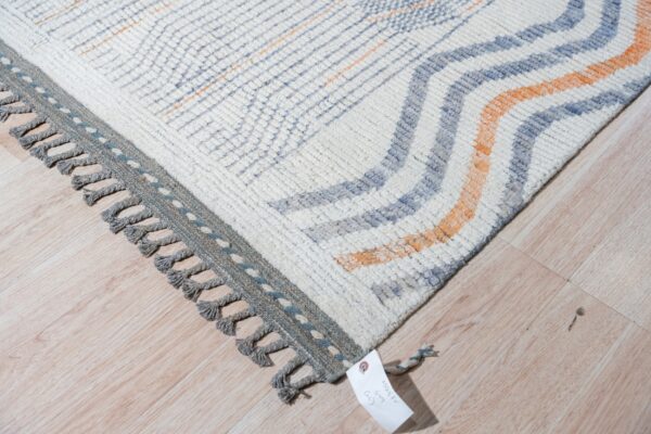 Textured cream rug featuring blue and orange wavy stripes, a gray border, and thick knotted tassels.