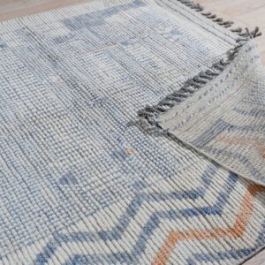 Chunky ribbed blue and cream rug with orange accents folded on light wood plank flooring.