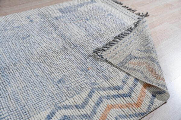 Chunky ribbed blue and cream rug with orange accents folded on light wood plank flooring.