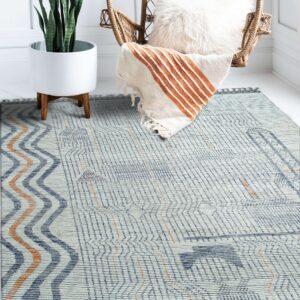 Blue, white, and rust geometric flatweave rug in a bright room with a wicker chair and potted plant.