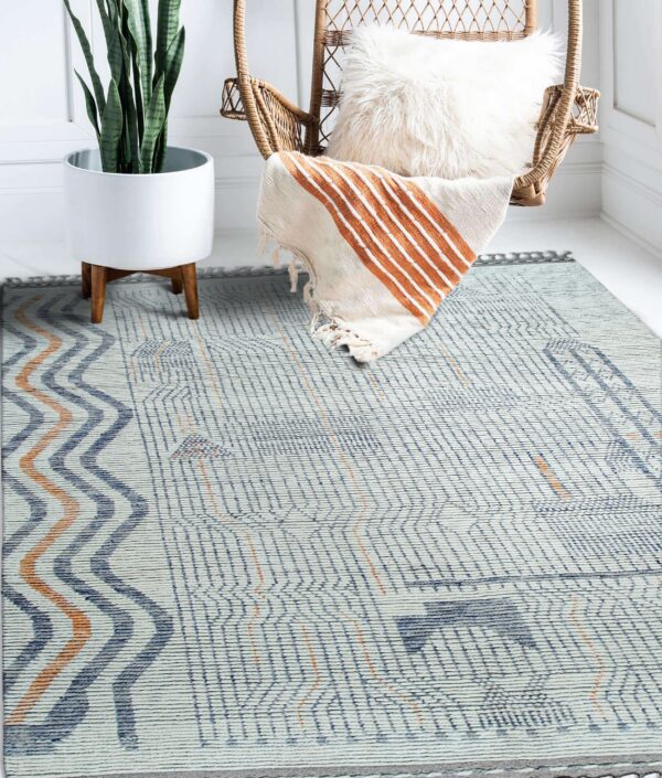 Blue, white, and rust geometric flatweave rug in a bright room with a wicker chair and potted plant.