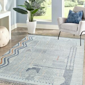 Geometric blue, gray, and orange textured rug with tassels anchors a bright room featuring an armchair.
