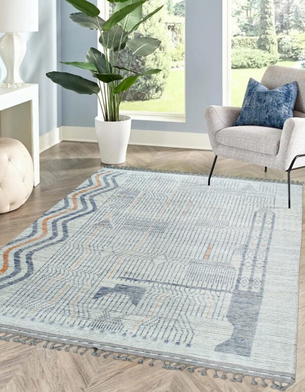 Geometric blue, gray, and orange textured rug with tassels anchors a bright room featuring an armchair.