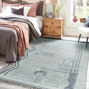 Light blue rug with fine-lined indigo and orange geometric designs sits below a bed and wooden nightstand.