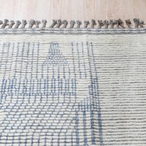 Textured cream rug with blue grid pattern, a visible orange stripe, and gray knotted fringe on wood floor.