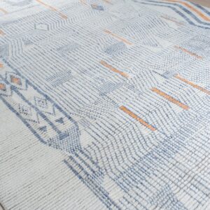 High-pile rug featuring blue geometric patterns and orange dashes over a creamy white textured surface.