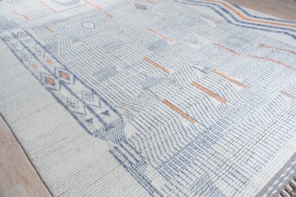High-pile rug featuring blue geometric patterns and orange dashes over a creamy white textured surface.