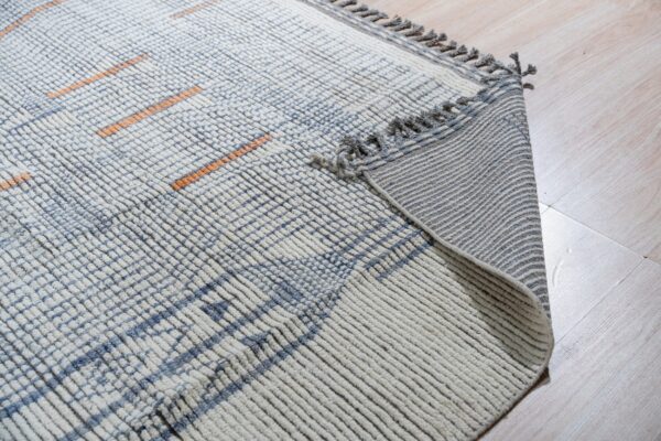 High-pile cream and blue ribbed rug with orange lines, showing the fringed backing on light wood flooring.