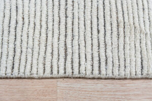The high-pile, ivory-toned rug has vertical ribs and dark stripes, seen against light wood flooring.