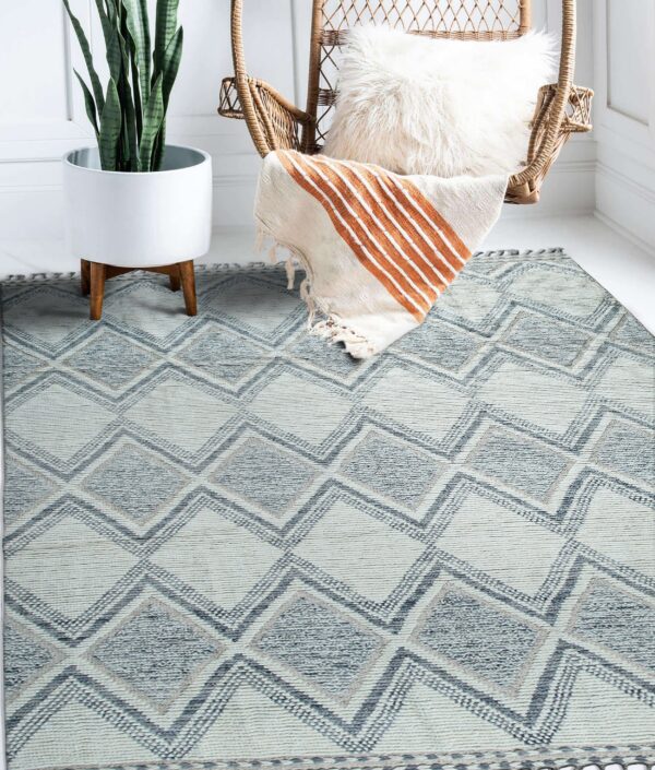 Blue and cream geometric rug with textured diamond pattern, styled next to a wicker chair and potted plant.