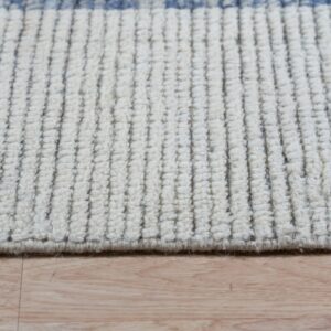 Close view of a cream ribbed rug featuring thin vertical dark threads and blue pattern accents on a wood floor.