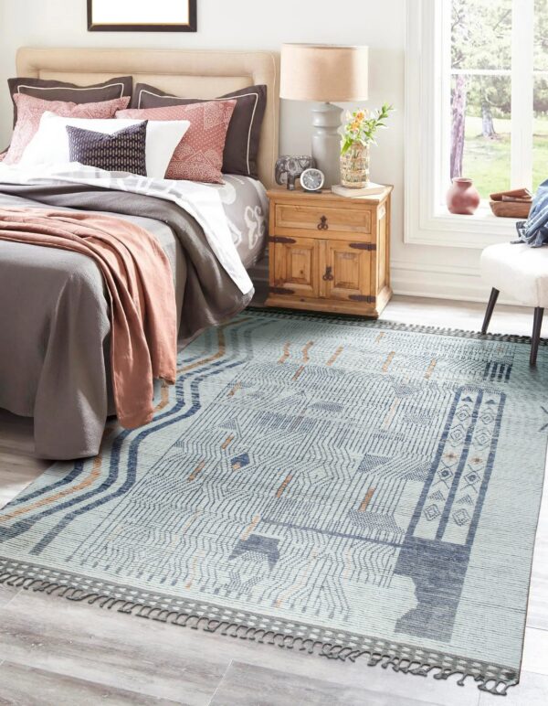 Pale blue geometric rug with dense indigo patterns and rust accents placed beside a wooden nightstand in a bedroom.