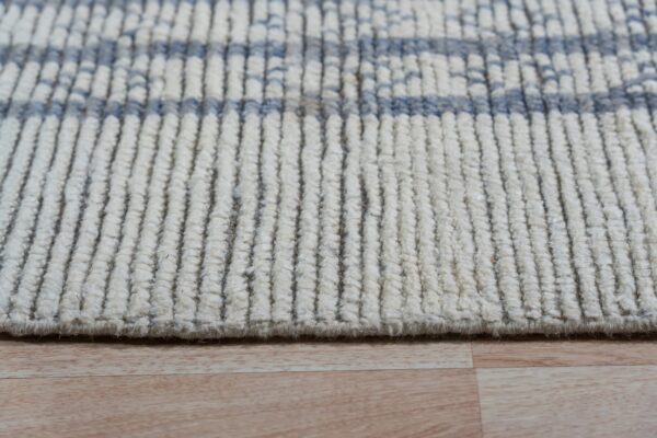 Close-up of a cream rug with vertical ribbed texture and light blue horizontal bands on light wood flooring.