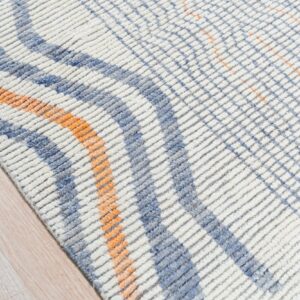 Textured white rug with blue and orange intersecting patterns rests on light blonde wood flooring.