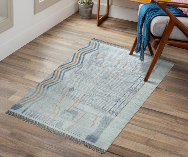 Low-pile rug with light blue, indigo, and orange abstract designs sits on wood plank flooring.