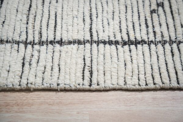 Chunky ivory high-pile rug with vertical black stripes detailed on light wood flooring.