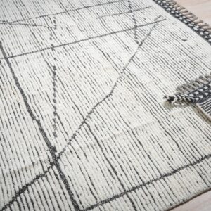 Textured high-pile cream rug with black abstract lines, revealing a striped backing and fringed edge.
