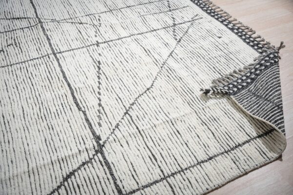 Textured high-pile cream rug with black abstract lines, revealing a striped backing and fringed edge.