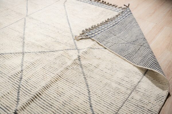 High-pile cream rug with gray diamonds is folded, showing its striped backing on light wood floor.