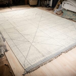 Large cream rug with light gray geometric intersecting lines and decorative tassels on a wood floor.