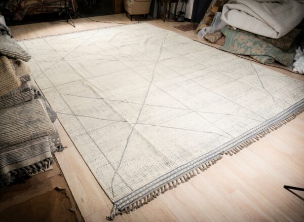 Large cream rug with light gray geometric intersecting lines and decorative tassels on a wood floor.