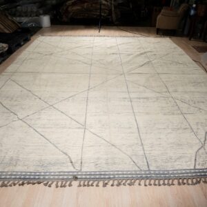 Off-white textured rug with thin gray geometric lines and tassels lying on light wood flooring.