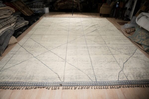 Off-white textured rug with thin gray geometric lines and tassels lying on light wood flooring.