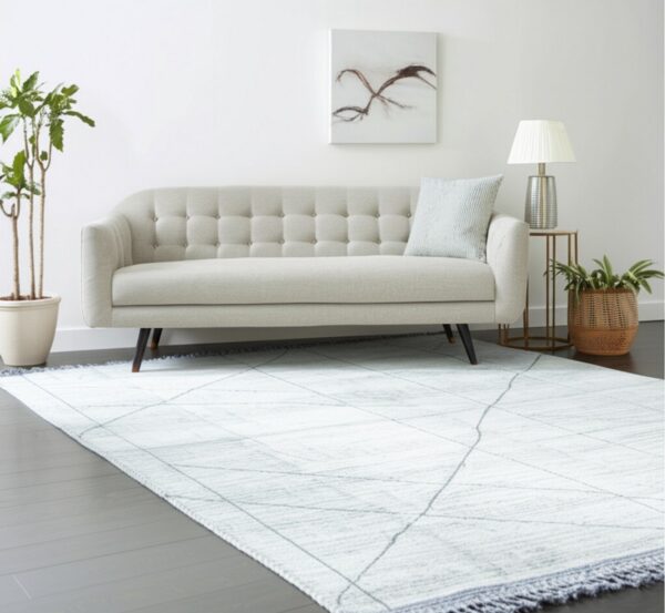 Light white rug with gray diagonal lines under a beige tufted sofa on dark wood flooring.
