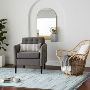 Blue flatweave rug with an abstract linear pattern beneath a gray armchair and wicker chair.