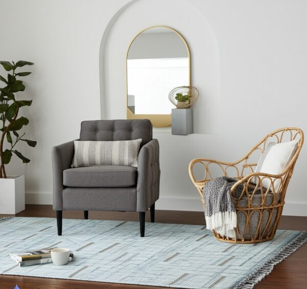 Blue flatweave rug with an abstract linear pattern beneath a gray armchair and wicker chair.
