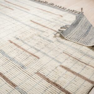 Cream high-pile rug with distinct vertical ribbing and brown and gray intersecting stripes on wood flooring.