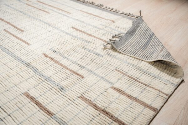 Cream high-pile rug with distinct vertical ribbing and brown and gray intersecting stripes on wood flooring.