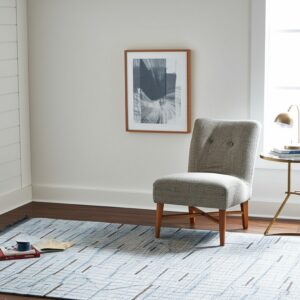 Blue and white textured flatweave rug with linear patterns under a gray chair and brass side table.
