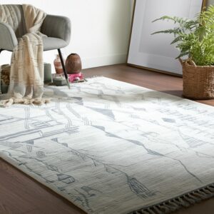 White low-pile rug with a blue abstract line drawing pattern next to a chair on dark wood floors.