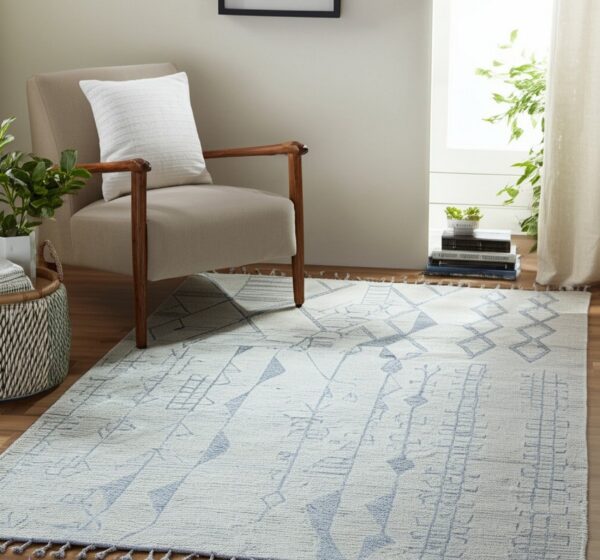 Light gray geometric rug with blue patterns and tassels placed under a neutral upholstered chair.