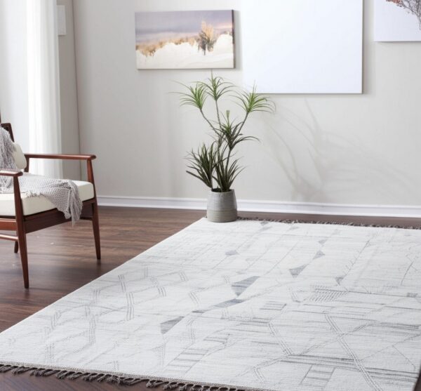 Light gray geometric rug with tassels on a dark wood floor, next to a wooden armchair and potted plant.