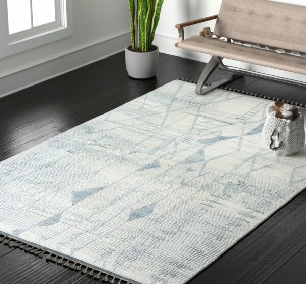 Light blue and white geometric rug with dark tassels contrasts with the black wood floor and tan bench.