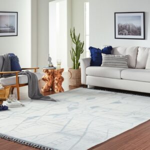 A large off-white rug with light blue geometric patterns and fringe rests on a hardwood floor beneath a white sofa.