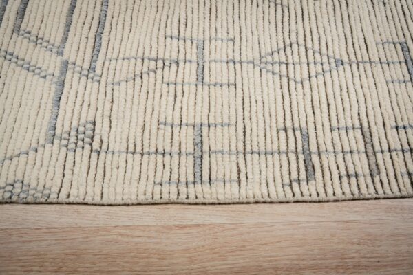 Close view of a cream, high-pile rug with a gray geometric pattern resting on light wood floor.