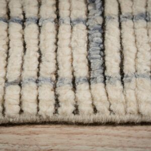 Extreme close-up showing thick, shaggy cream pile with dark vertical lines and intersecting blue bands on wood flooring.
